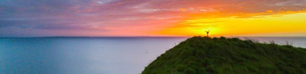 Sunset over Biliran Island with a traveler on the hill, vibrant sky over the ocean