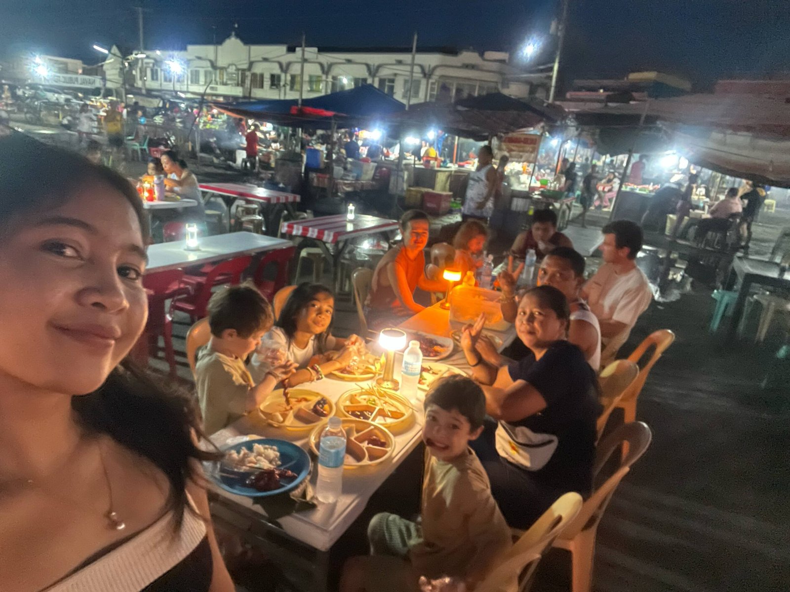 Dinner at a Filipino night market with locals and travelers, sharing food and smiles under warm lights.